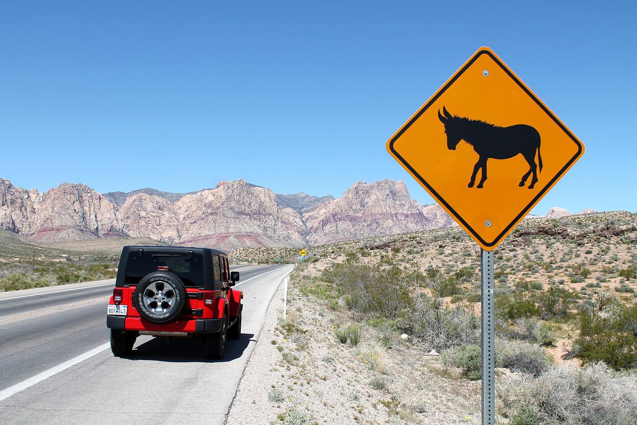 Red Jeep Wrangler driving down a desert road.